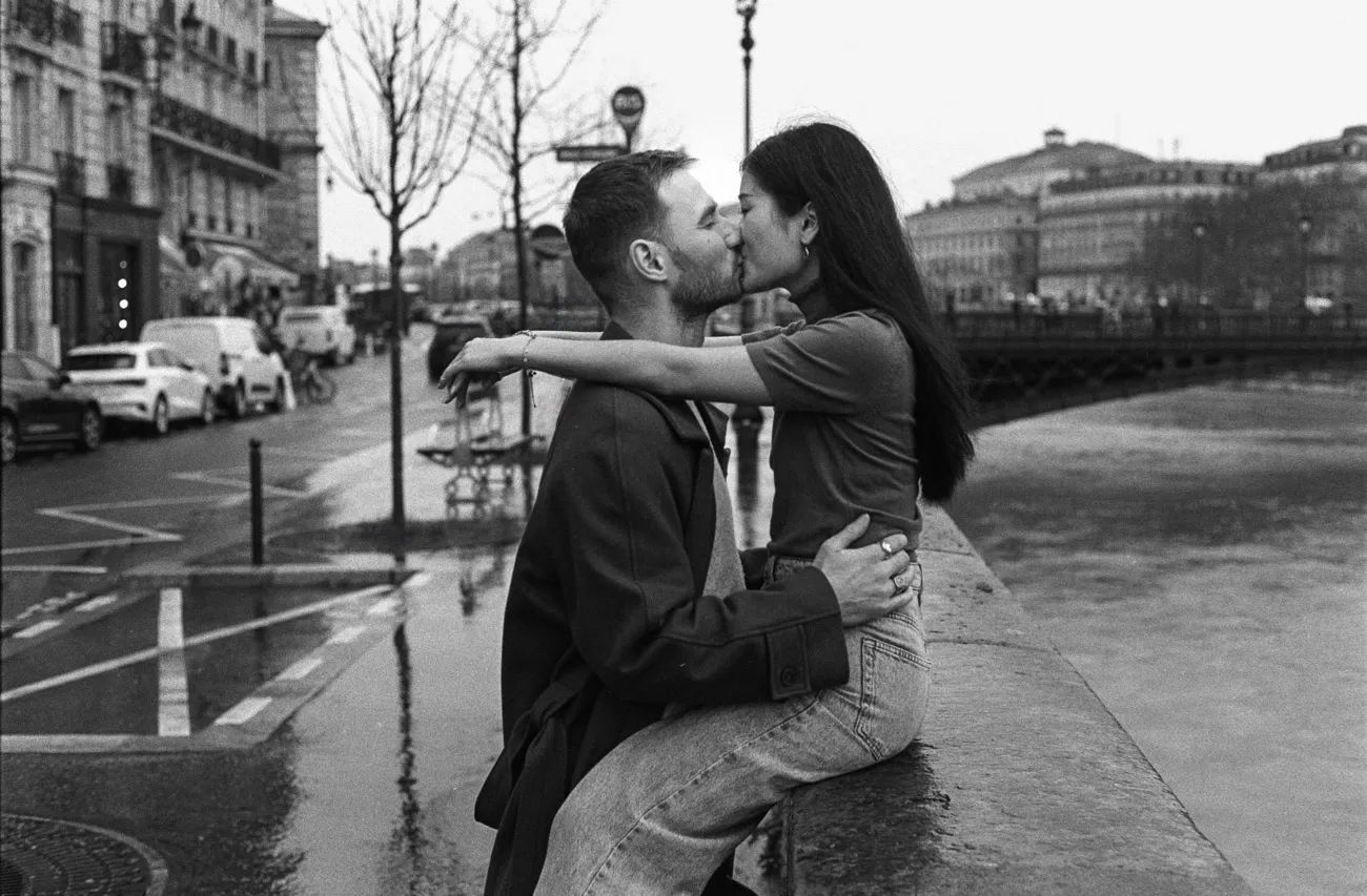 Couple kissing on a stone wall beside the Seine on a grey morning, in black and white