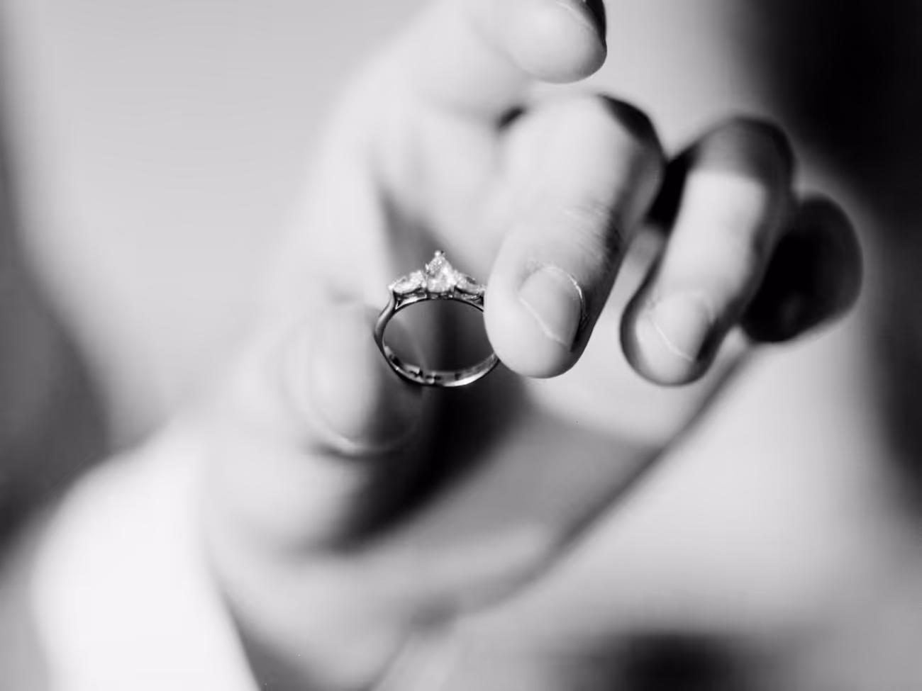 Close detail of a hand holding up an engagement ring, shot on black and white film