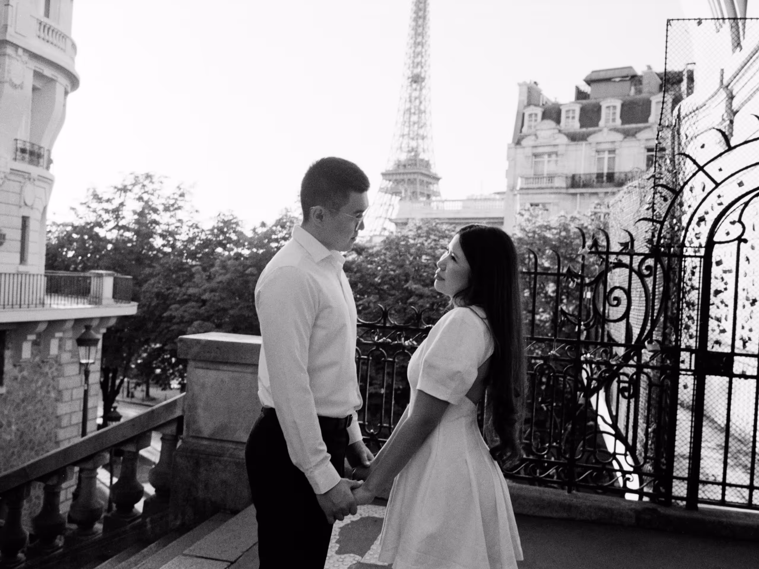 Couple holding hands on a Paris terrace with the Eiffel Tower behind them, shot on black and white film