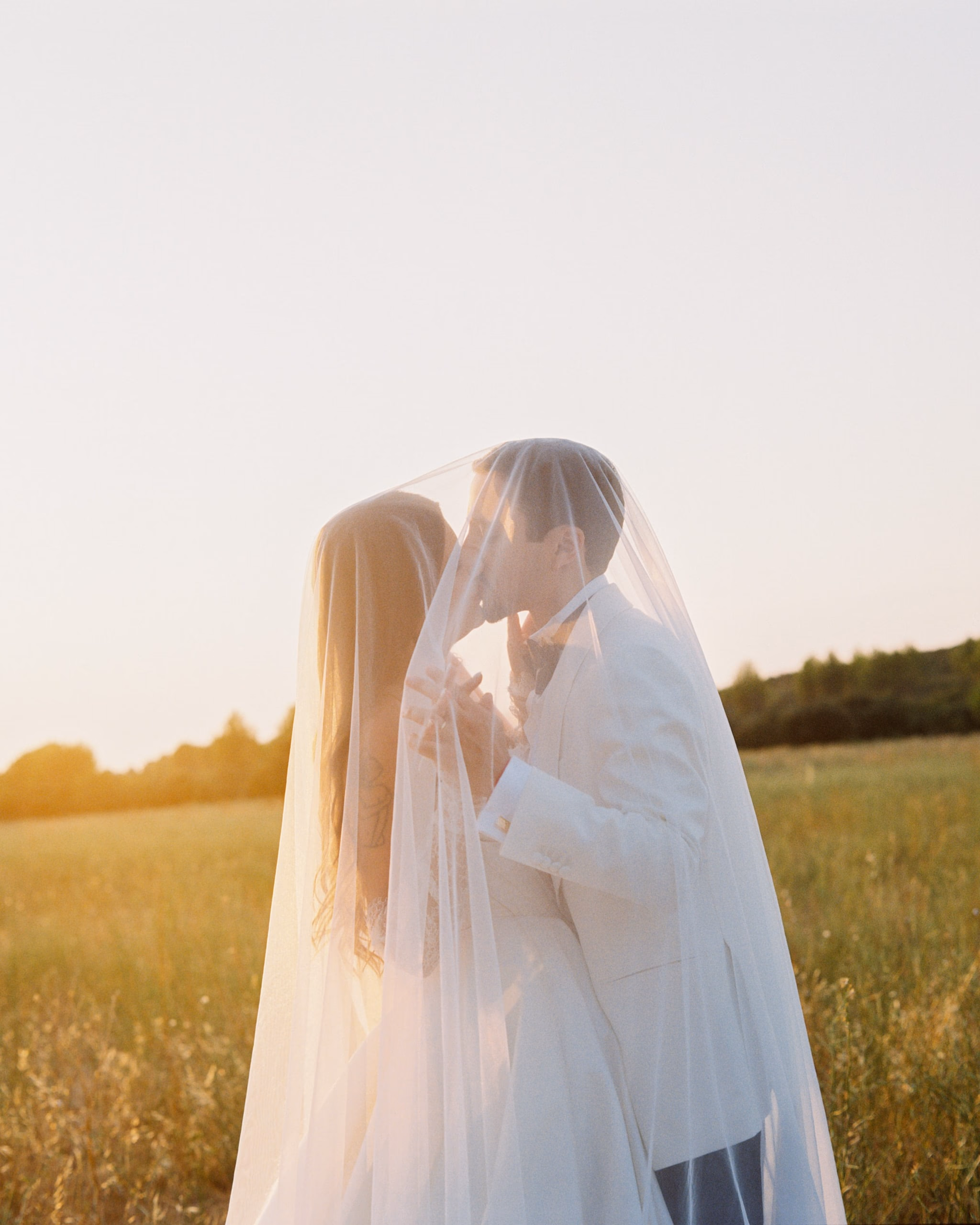 Bride and groom kissing beneath her veil in a golden field at sunset, south of france, provence, wedding, bastide d'astres, aix en provence, shot on film, film photography, analog photography