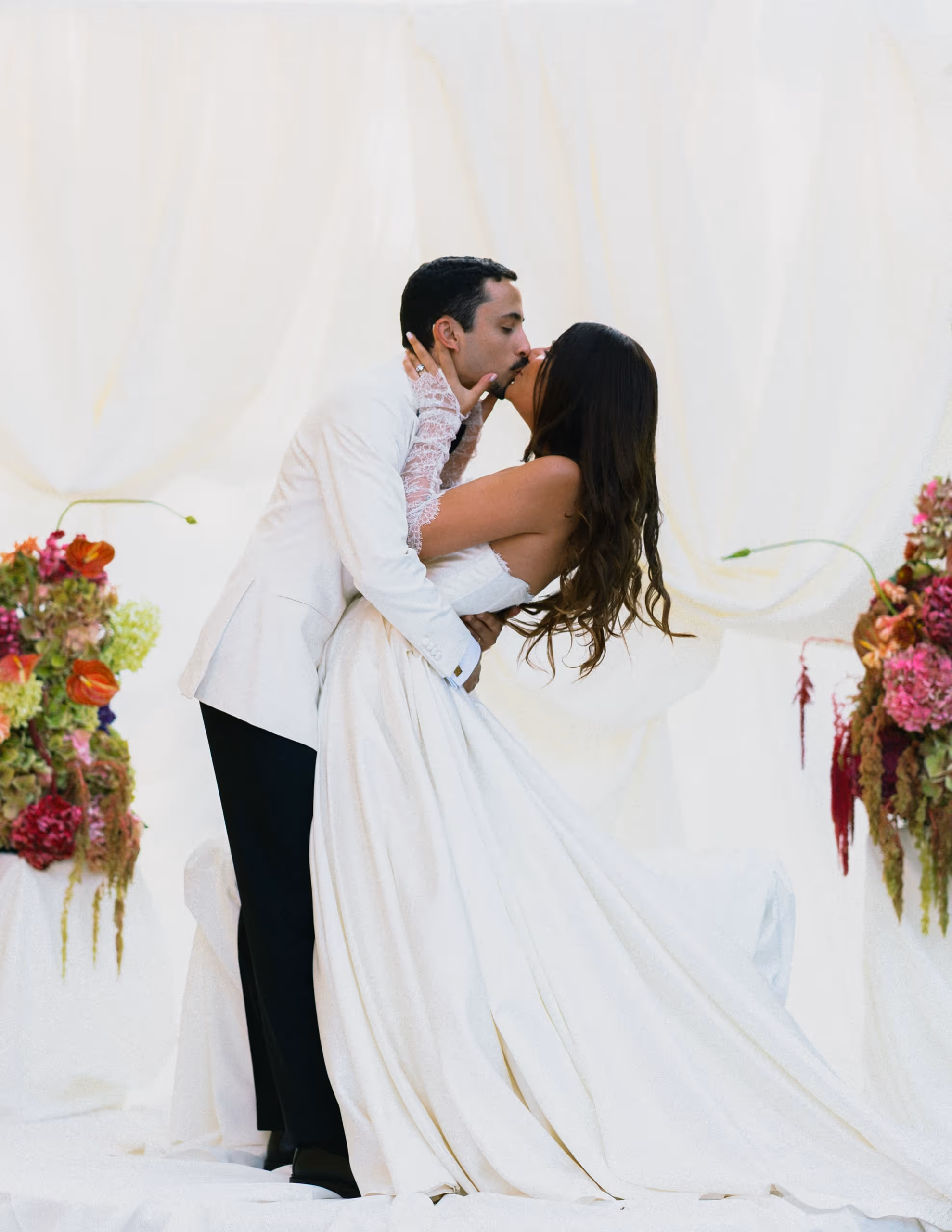 Bride and groom kissing between white drapes and banks of summer flowers, provence wedding, south of france