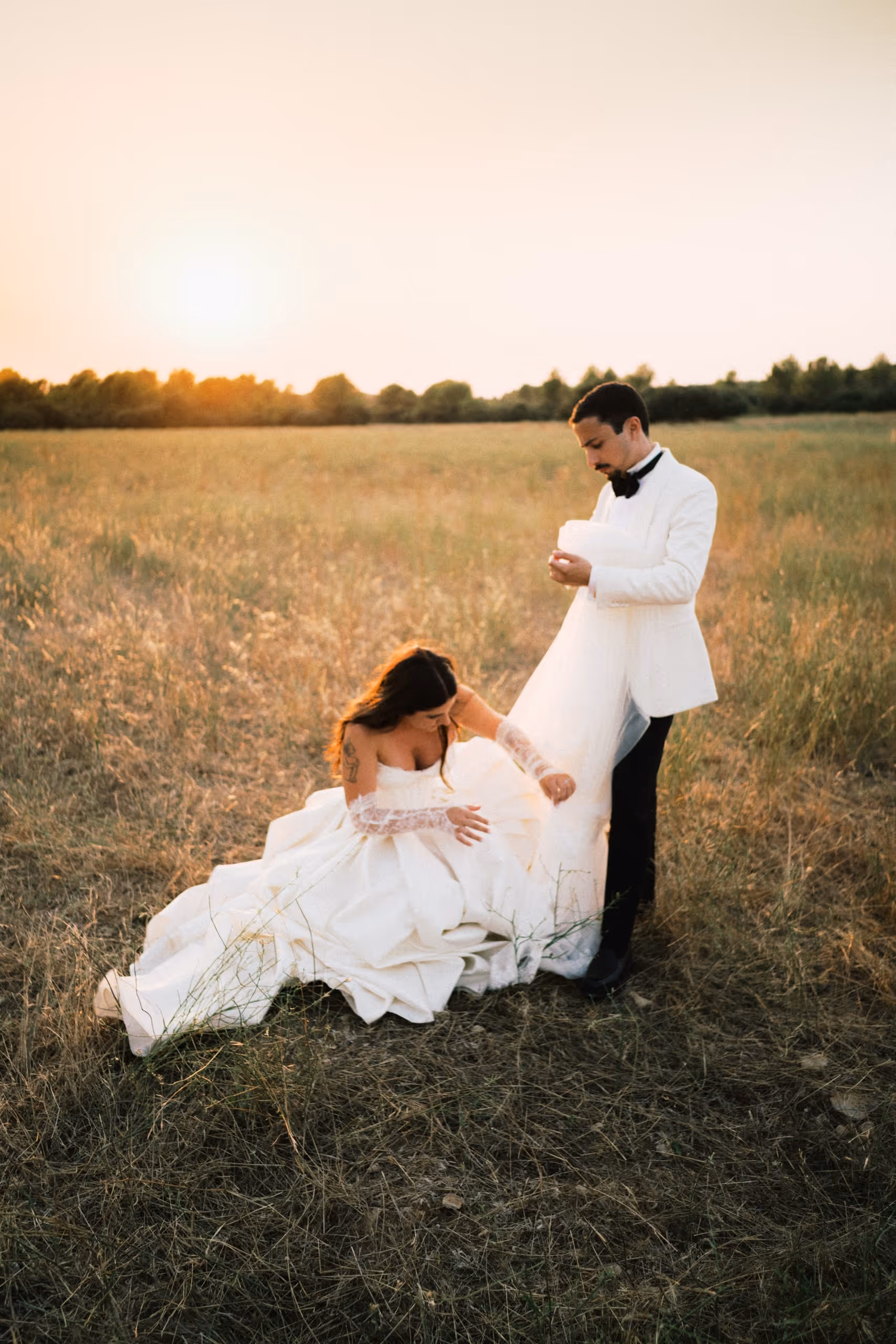 Bride seated in a golden field at sunset, her groom standing over her, south of france wedding, provence