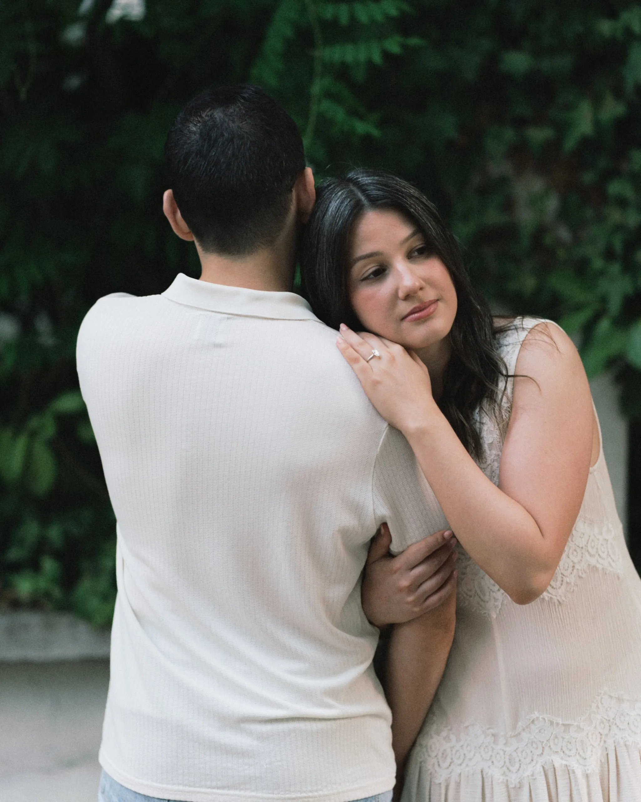 Couple embracing against green leaves in Montmartre, her cheek resting on his shoulder