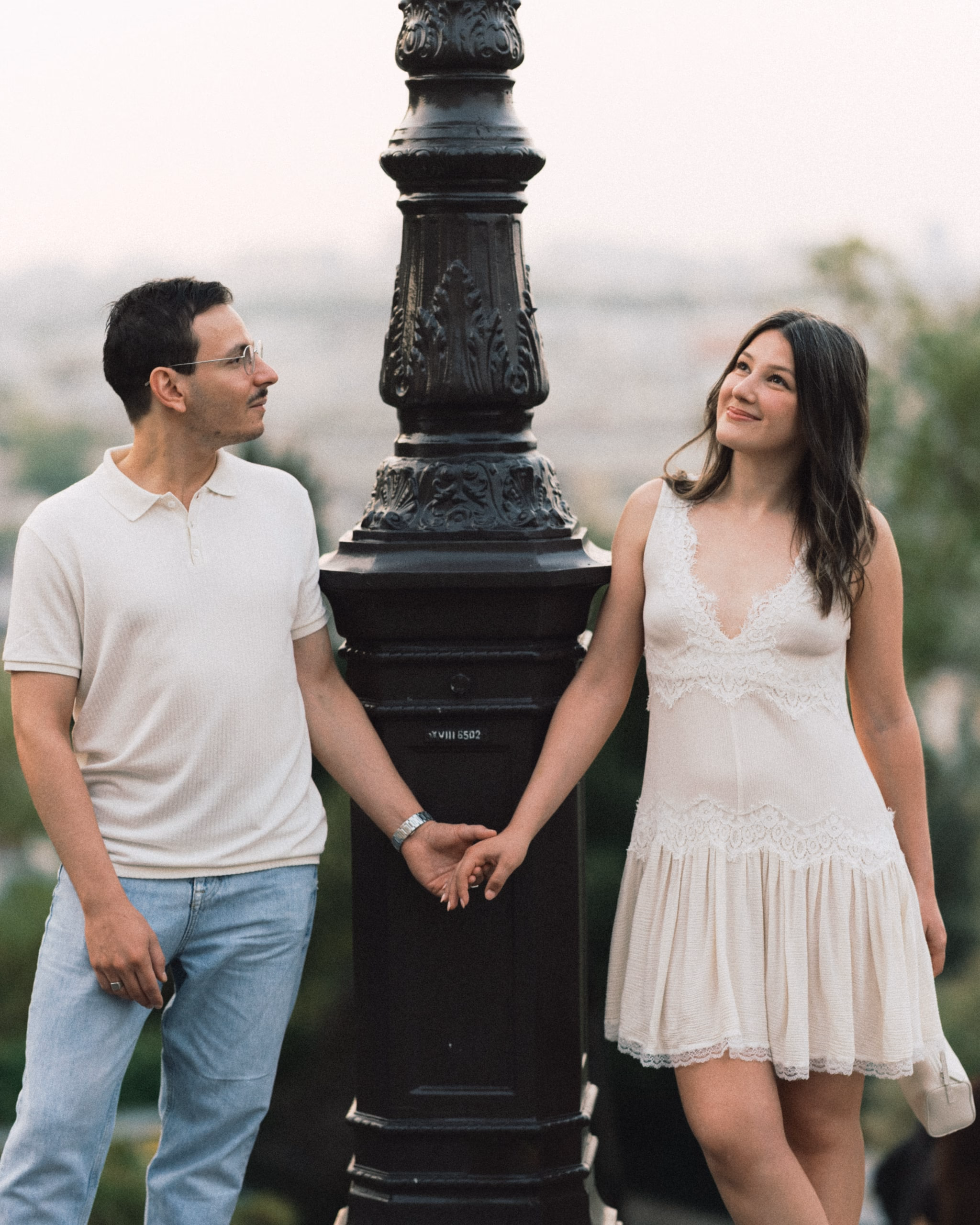 Couple joining hands around a lamppost above the Paris rooftops in Montmartre