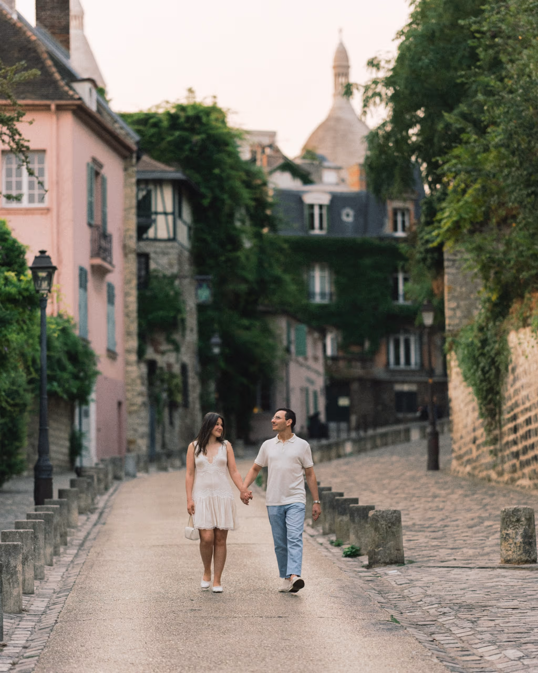 Couple walking hand in hand down a cobbled Montmartre street with the dome of Sacré-Cœur behind them