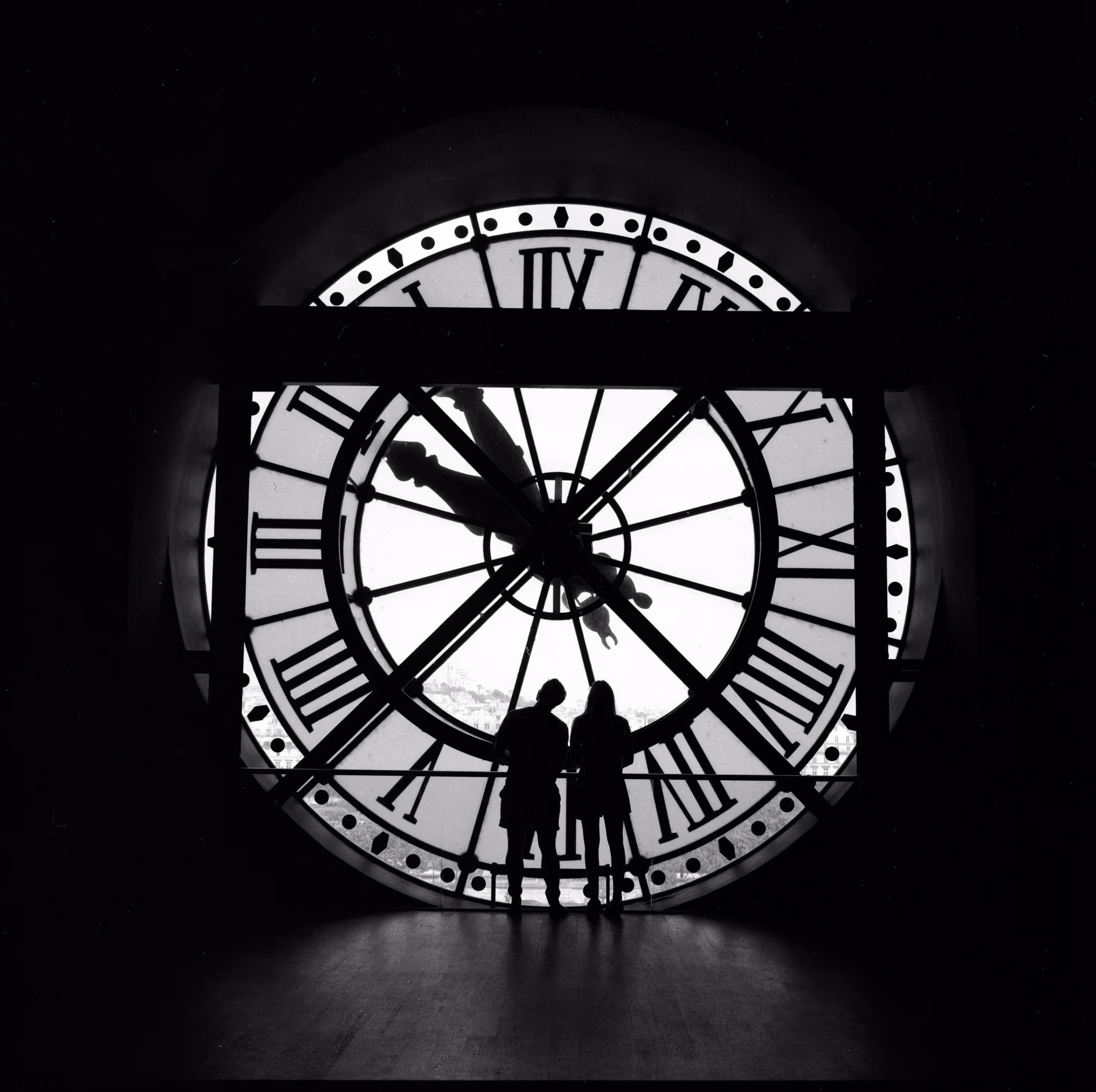 Two figures silhouetted against the great glass clock of the Musee d'Orsay, the city visible through it, shot on medium-format film