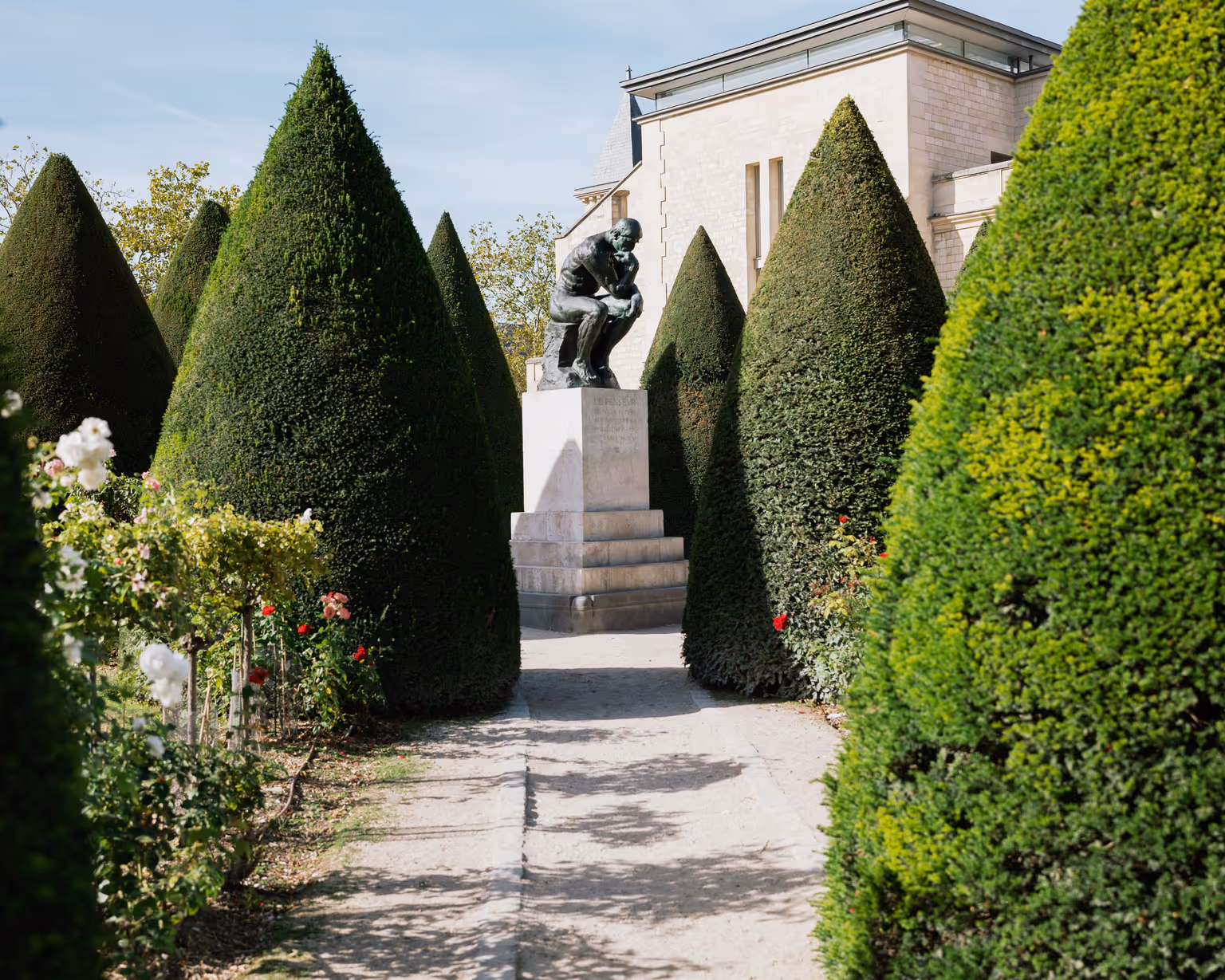 A garden path at the Musée Rodin, with trees and a bronze sculpture in front of the building.
