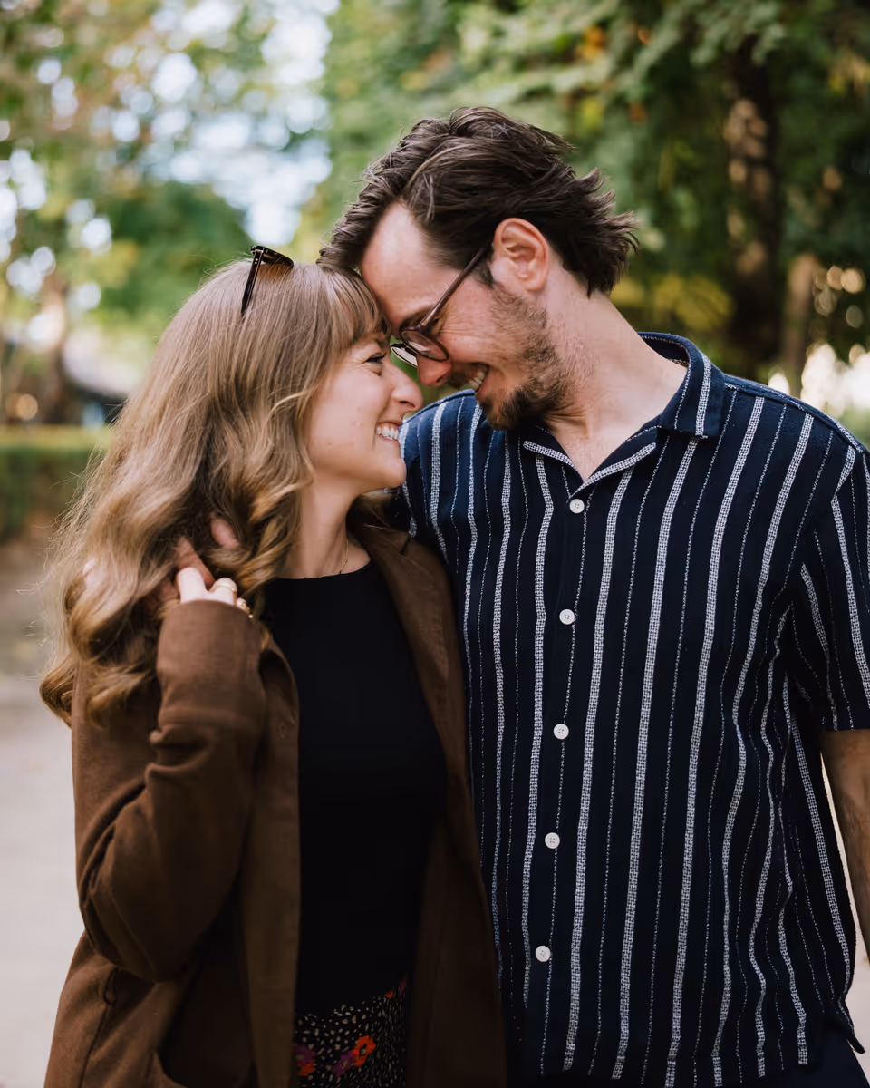 Paige and Reinhardt smiling with their foreheads touching in front of garden greenery.