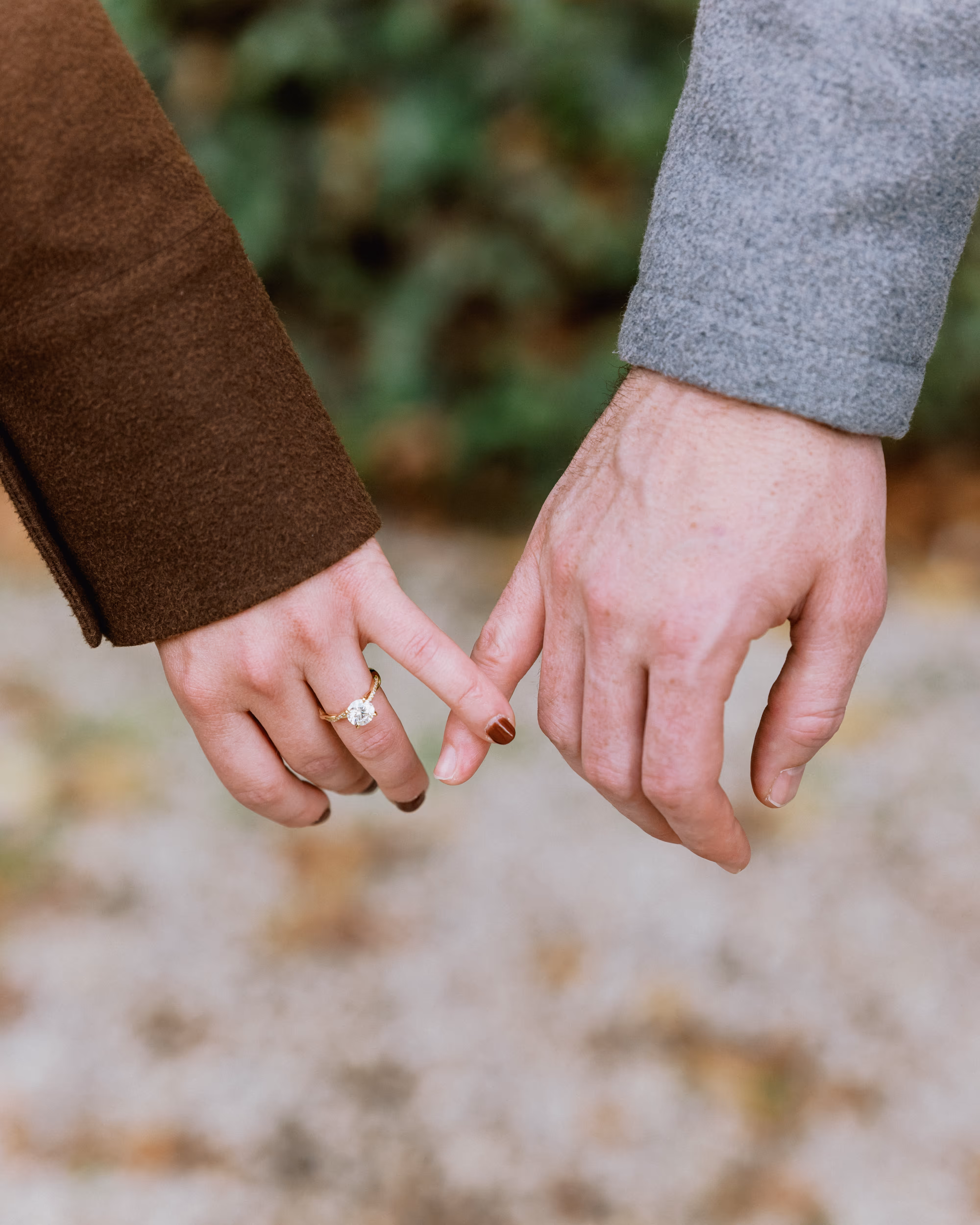 Close view of Paige and Reinhardt linking their little fingers, with Paige's engagement ring visible beside her brown jacket sleeve.