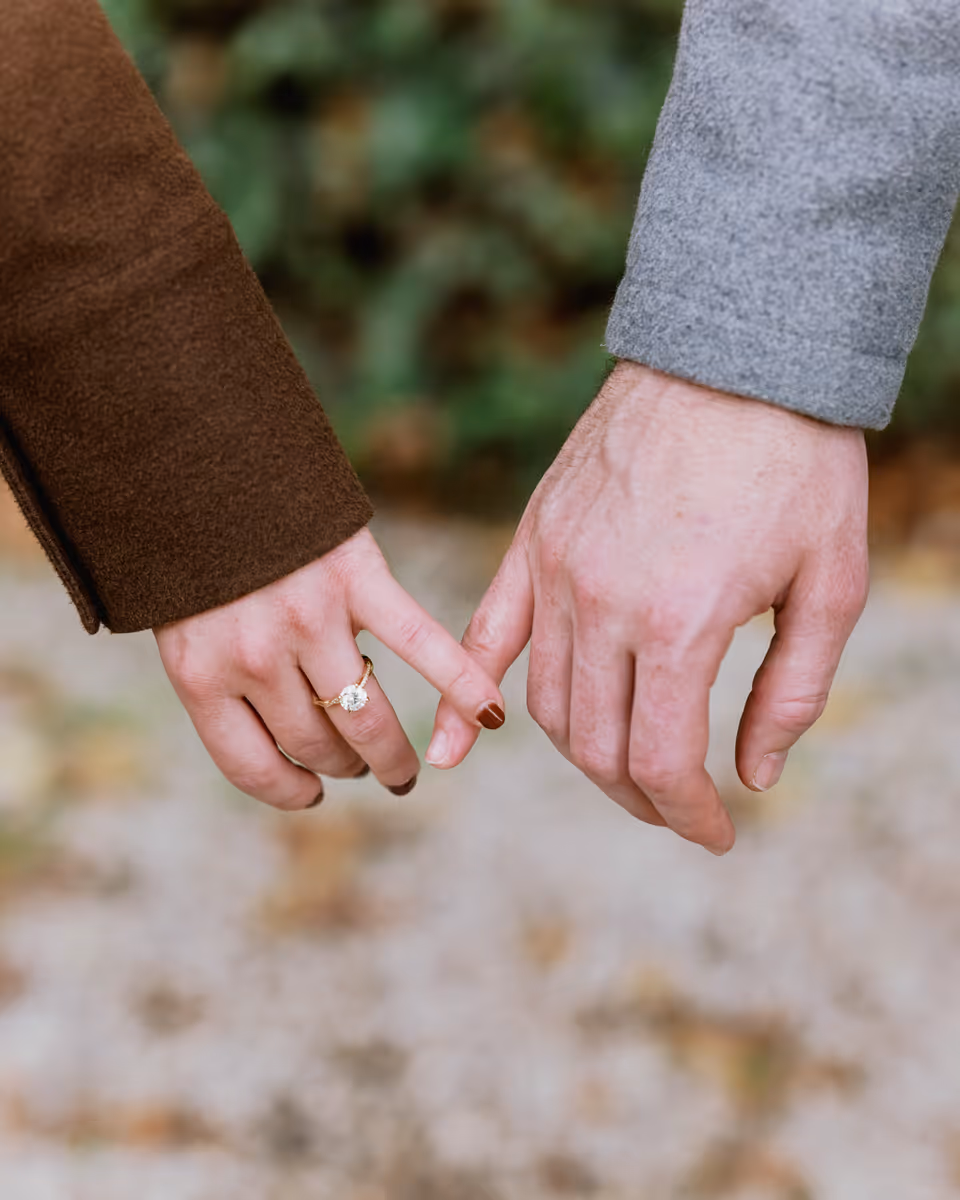 Close view of Paige and Reinhardt linking their little fingers, with Paige's ring visible beside her brown jacket sleeve.