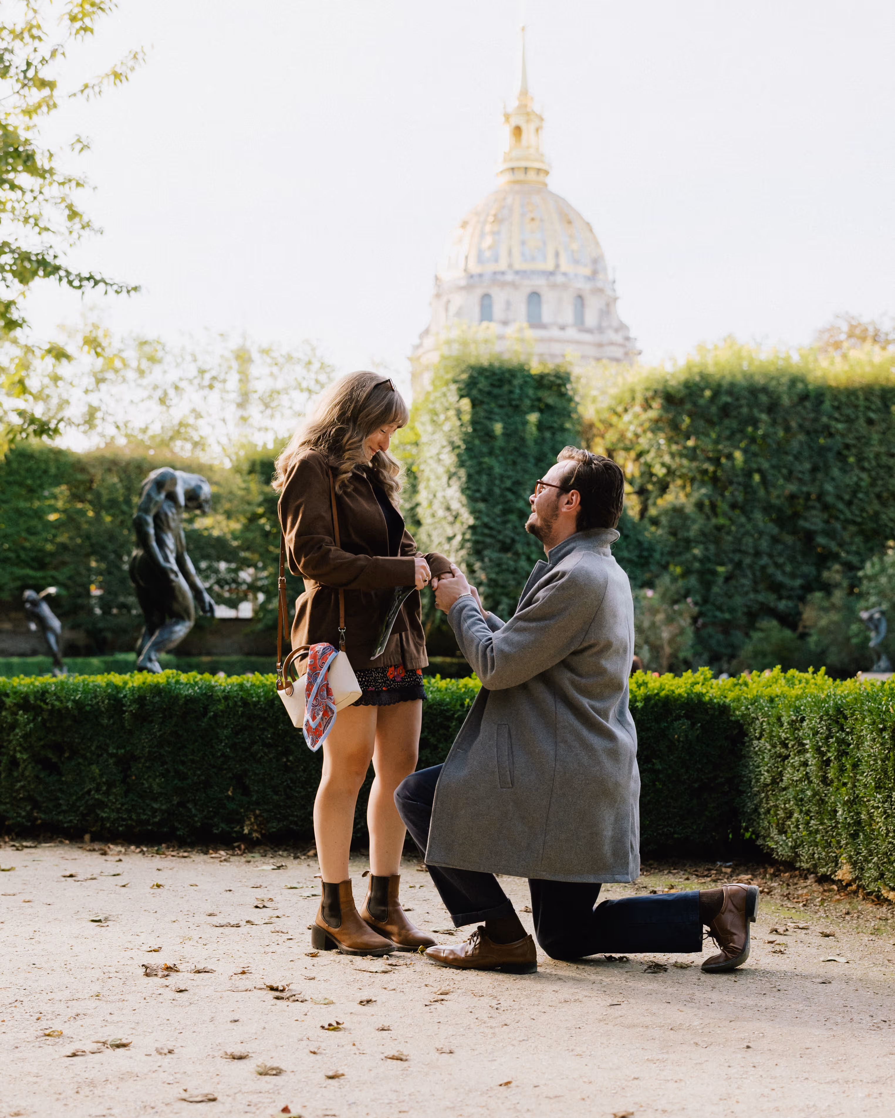 Reinhardt proposing to Paige in the Musée Rodin garden, with the Invalides dome behind them.