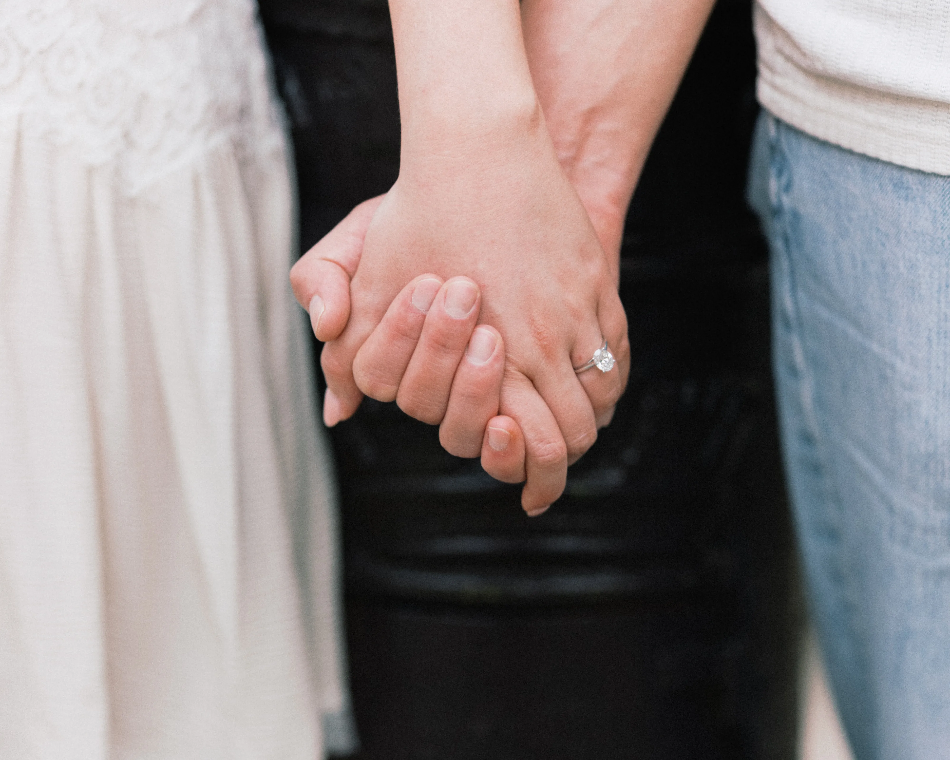 Close-up of a couple holding hands, her engagement ring catching the light