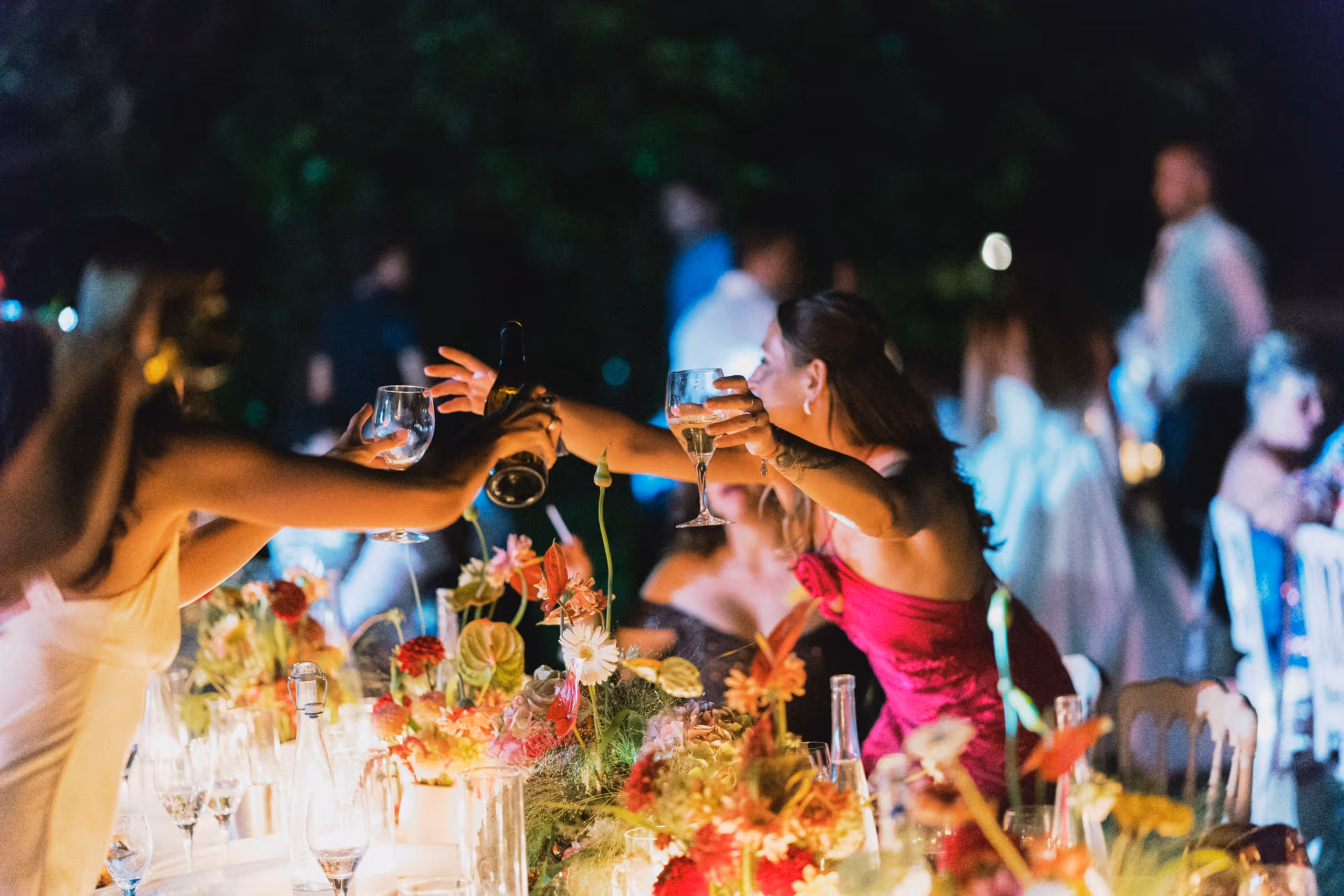 Guests reaching across the table to clink glasses at the outdoor reception after dark