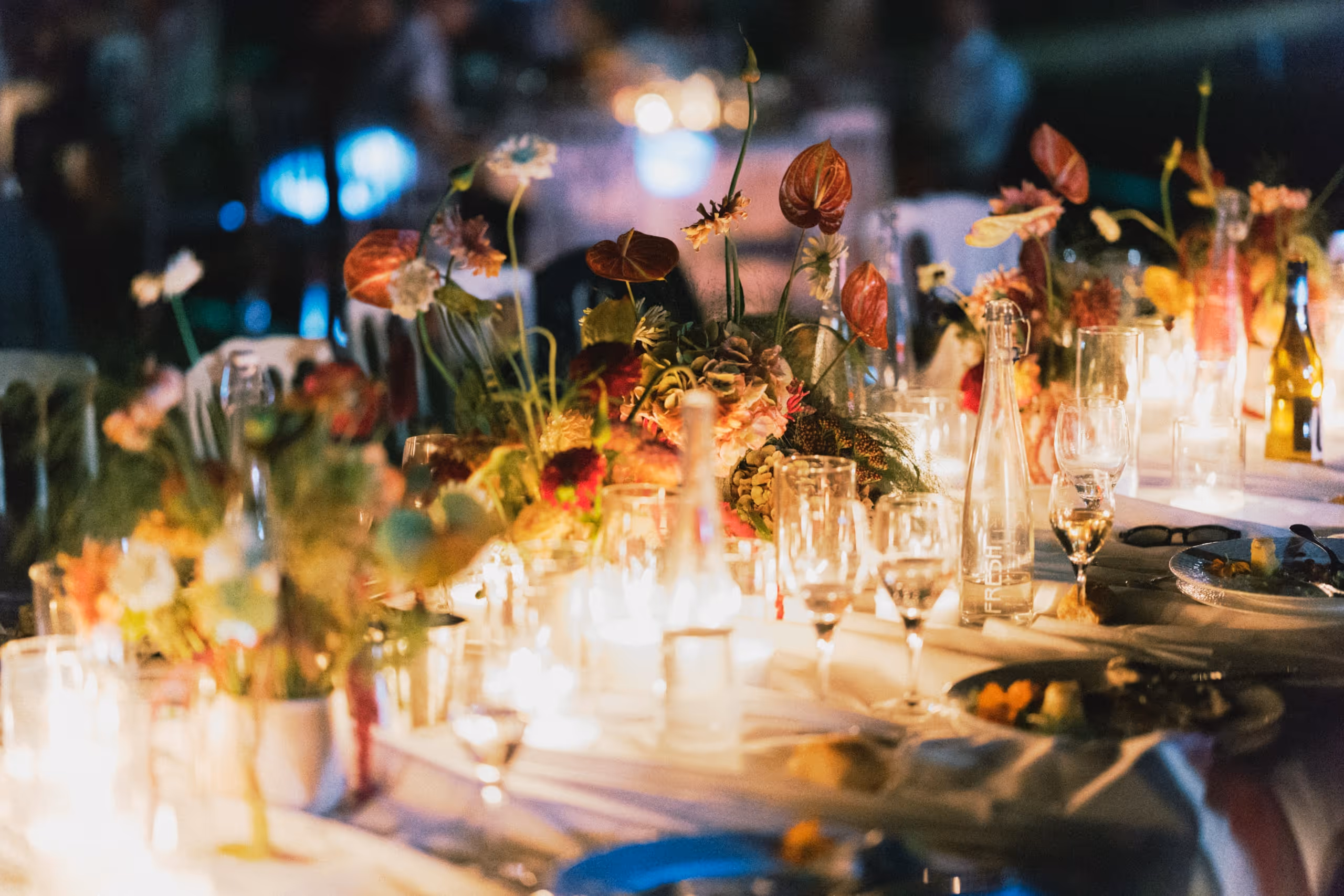 Long reception table by candlelight at night, dense with summer flowers